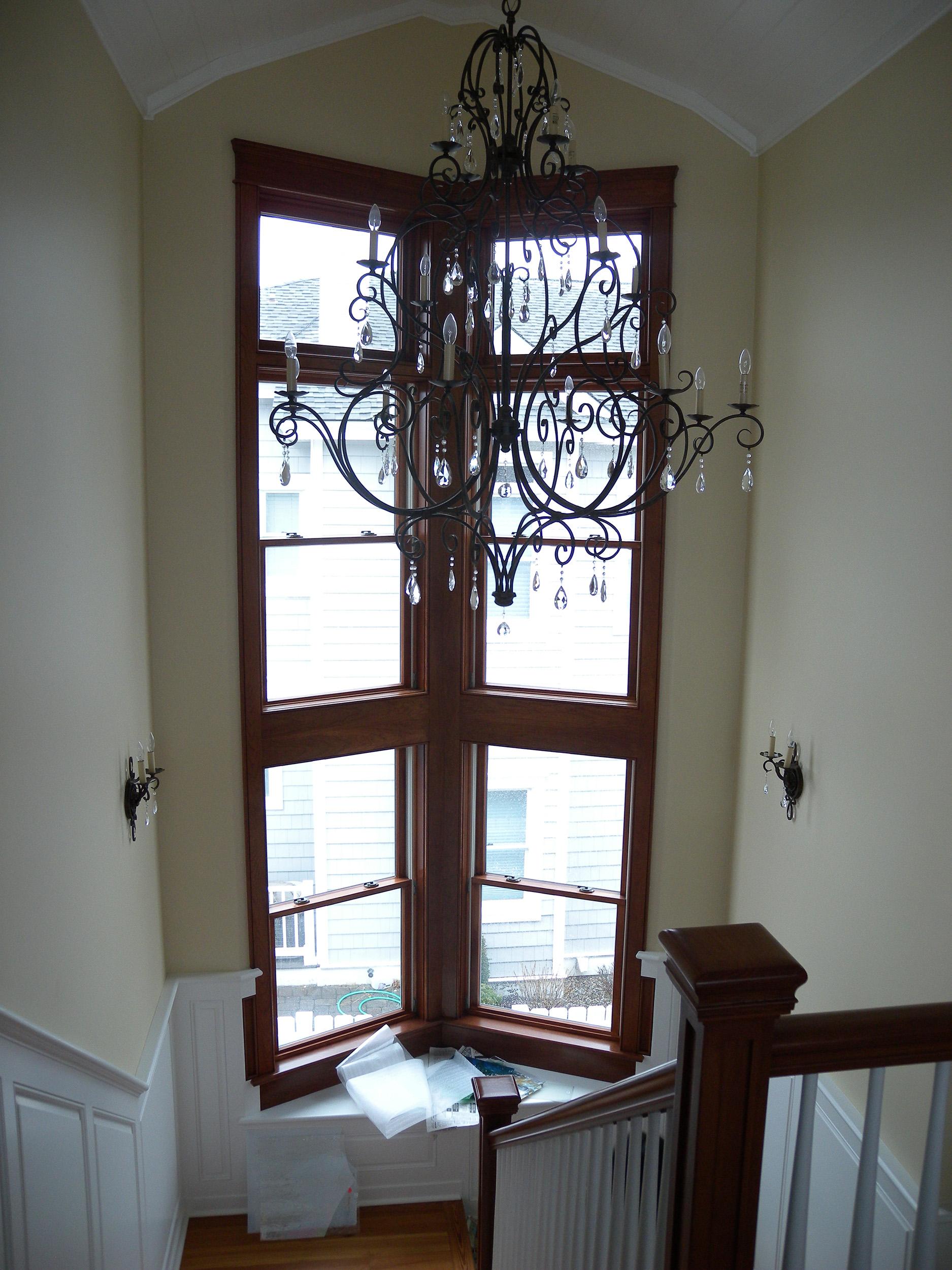 A two-story high, stacked staircase window in the grand entry hall in a residential coastal house. Made with a rich, dark wood trim.