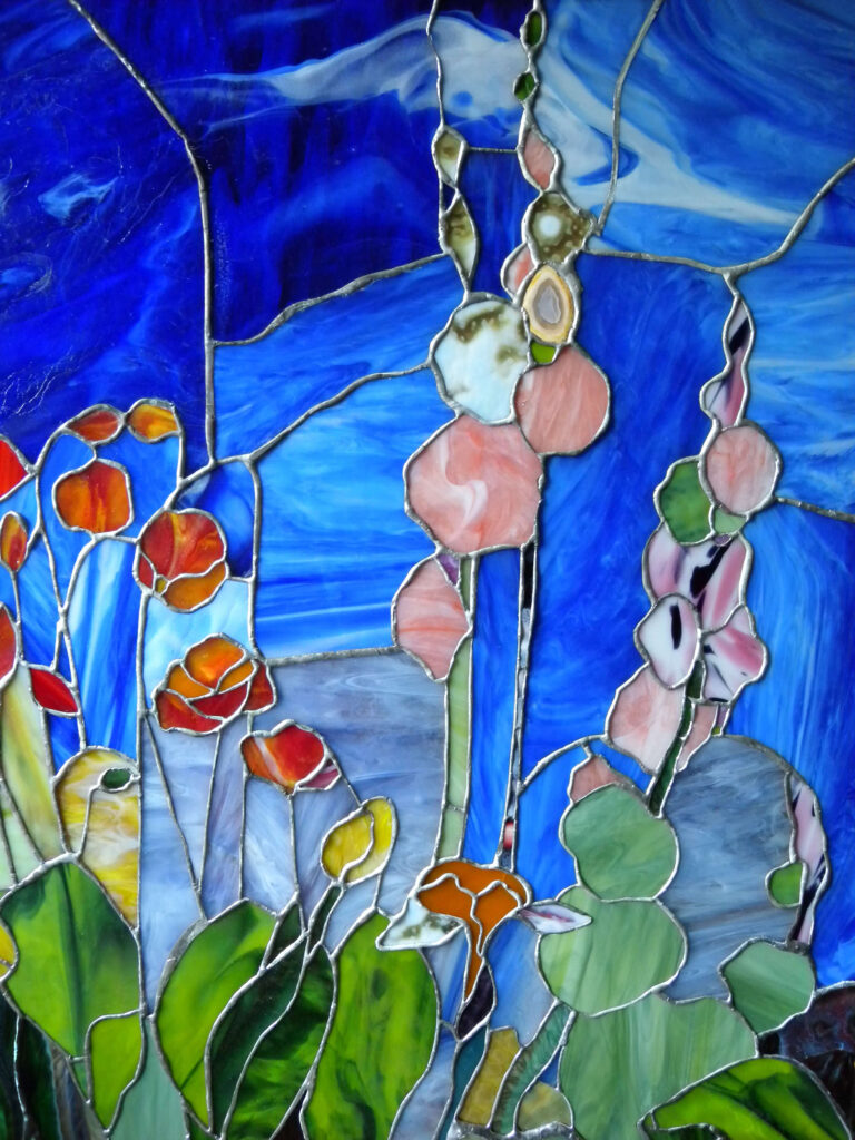 Modern glass art showcasing a vibrant garden with detailed floral patterns, including irises and California poppies, set against a cobalt blue sky. The style echoes Louis Tiffany, featuring diverse textures and bright colors of opalescent glass.